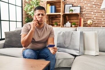 Canvas Print - Hispanic young man doing payment with credit card on the phone looking at the camera blowing a kiss being lovely and sexy. love expression.