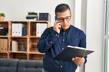 Wall Mural - Young latin man business worker talking on smartphone reading document at office