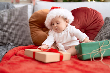 Canvas Print - Adorable toddler wearing christmas hat sitting on sofa with present at home