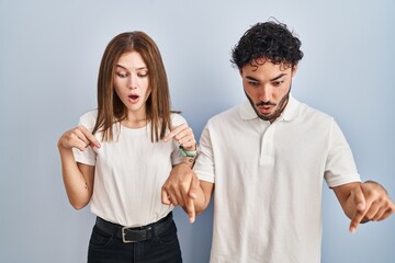 Canvas Print - Young couple wearing casual clothes standing together pointing down with fingers showing advertisement, surprised face and open mouth