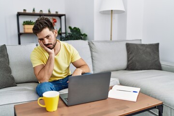 Canvas Print - Young man with beard using laptop at home thinking looking tired and bored with depression problems with crossed arms.