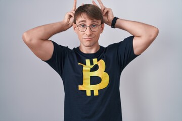 Sticker - Caucasian blond man wearing bitcoin t shirt posing funny and crazy with fingers on head as bunny ears, smiling cheerful