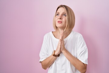 Sticker - Young caucasian woman standing over pink background begging and praying with hands together with hope expression on face very emotional and worried. begging.