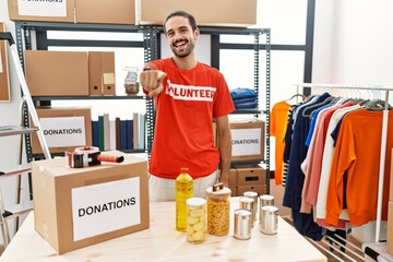 Poster - Young hispanic man wearing volunteer t shirt at donations stand pointing to you and the camera with fingers, smiling positive and cheerful