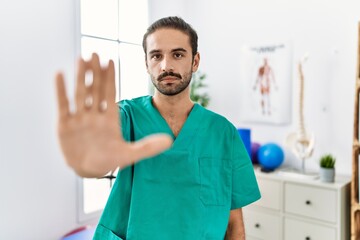 Sticker - Young physiotherapist working at pain recovery clinic doing stop sing with palm of the hand. warning expression with negative and serious gesture on the face.