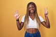 African american woman with braided hair standing over yellow background showing and pointing up with fingers number seven while smiling confident and happy.