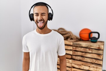 Wall Mural - African american man listening to music using headphones at the gym sticking tongue out happy with funny expression. emotion concept.