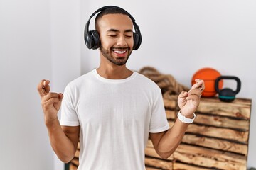 Poster - African american man listening to music using headphones at the gym gesturing finger crossed smiling with hope and eyes closed. luck and superstitious concept.