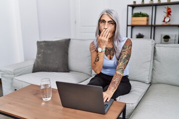 Sticker - Middle age grey-haired woman using laptop at home bored yawning tired covering mouth with hand. restless and sleepiness.