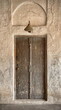 Aged, antique style brown door from Middle East set against tradition mud stone walls. Copper style overhead light. 