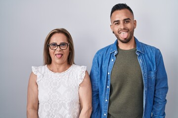 Sticker - Hispanic mother and son standing together sticking tongue out happy with funny expression. emotion concept.