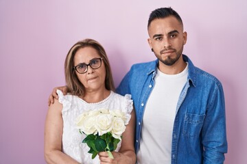 Poster - Hispanic mother and son together holding bouquet of white flowers relaxed with serious expression on face. simple and natural looking at the camera.