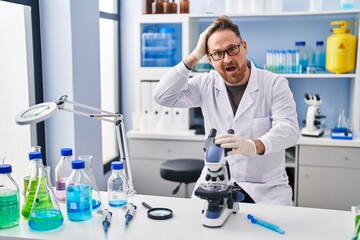 Canvas Print - Middle age caucasian man working at scientist laboratory stressed and frustrated with hand on head, surprised and angry face