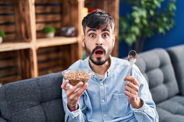 Poster - Young hispanic man with beard eating healthy whole grain cereals afraid and shocked with surprise and amazed expression, fear and excited face.