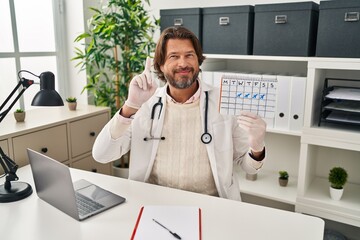 Wall Mural - Handsome middle age doctor man holding holidays calendar surprised with an idea or question pointing finger with happy face, number one