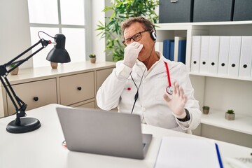 Canvas Print - Senior doctor man working on online appointment smelling something stinky and disgusting, intolerable smell, holding breath with fingers on nose. bad smell