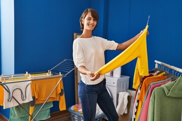 Wall Mural - Young beautiful hispanic woman smiling confident holding sweater on clothes rack at laundry room