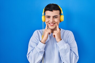 Poster - Non binary person listening to music using headphones smiling with open mouth, fingers pointing and forcing cheerful smile