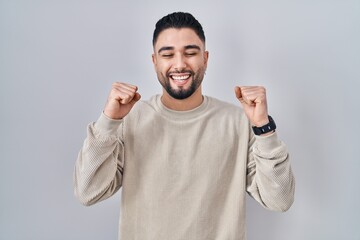 Poster - Young handsome man standing over isolated background excited for success with arms raised and eyes closed celebrating victory smiling. winner concept.