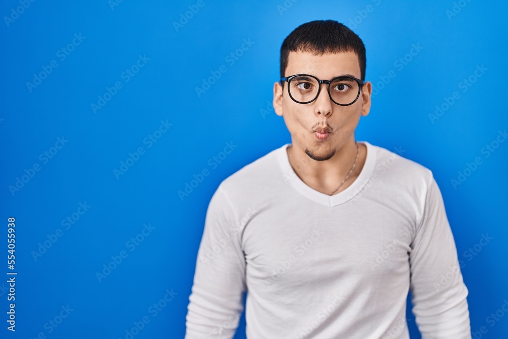 Young arab man wearing casual white shirt and glasses making fish face with lips, crazy and comical gesture. funny expression.