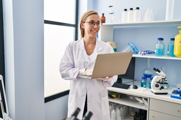 Wall Mural - Young blonde woman scientist smiling confident using laptop at laboratory