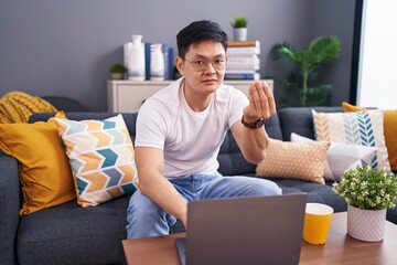 Canvas Print - Young asian man using laptop at home sitting on the sofa doing italian gesture with hand and fingers confident expression