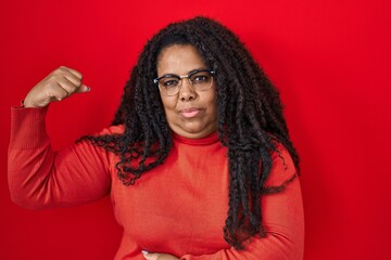 Poster - Plus size hispanic woman standing over red background strong person showing arm muscle, confident and proud of power