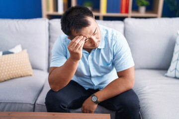 Wall Mural - Young chinese man stressed sitting on sofa at home