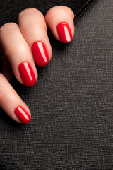 Wall Mural - Female hand with beautiful manicure - red nails on black leather surface background. Nail care concept
