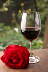 Wall Mural - Glass of red wine and rose flower on wooden table outdoors