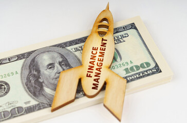 On the dollars lies a wooden model of a rocket with the inscription - FINANCE MANAGEMENT