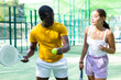 © JackF - African-american man padel trainer teaching young caucasian woman to serve ball on outdoor court.