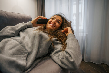 Teenager talking to her friends on the phone, laying on a couch after school, low angle shot