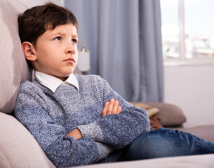 Upset preteen boy sitting at table and thinks about problems