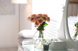 Glass vase with beautiful flowers on dressing table in modern room interior