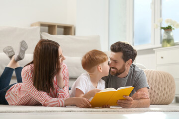 Happy parents with their child reading book on floor at home