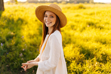 Wall Mural - front view of attractive happy young woman wearing straw hat and white dress standing posing on beau