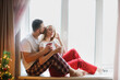 © natalialeb - Portrait of young man and woman drink coffee from mugs hugging and talking on window sill near window. Copy space.