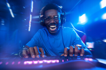 Happy American African Professional gamer, winner rejoices in victory of online games tournaments pc computer with headphones, blue background