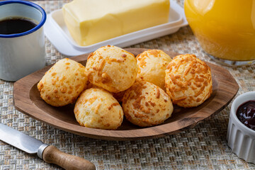 Wall Mural - Typical brazilian cheese bun in a plate with coffee, butter and orange juice over wooden table