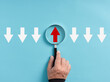© Cagkan - Focusing on business growth trend, development opportunity or positive aspects. Hand holds magnifying glass focusing on the red up arrow with different direction than the white down arrows.