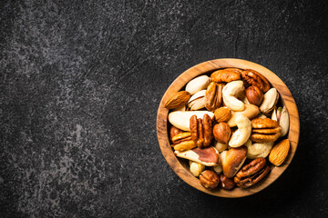 Wall Mural - Assortment of nuts in wooden bowl on dark stone table. Cashew, hazelnuts, almonds, brazilian nuts and pecans.