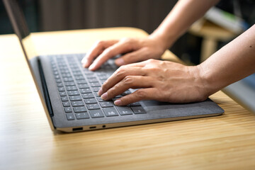 Wall Mural - Action of a businessperson is typing on the modern design laptop keyboard to input or program data, business working concept scene. Close-up and selective focus at human hand's part.