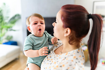 mother holding child baby on the living room. the baby is sick having some cough