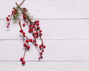 Wall Mural - Fir branch, with branches of red berries and snow. Christmas green spruce branch, decoration red berries holly on wooden light background with copy space.