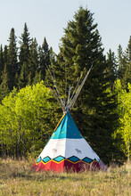 Decorative Painted Tipi In A Field With Trees In The Background And Blue Sky, West Of Turner Valley; Alberta, Canada