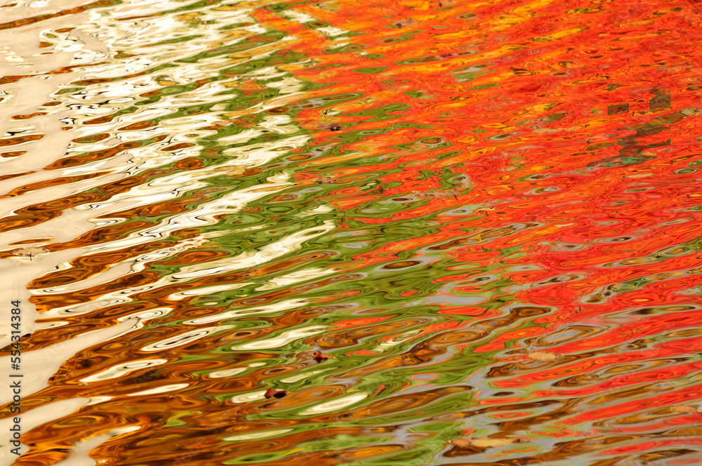 Colorful fall foliage reflected on the rippling surface of a pond ...