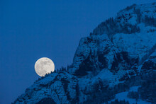 Full Moon Rising In A Blue, Night Sky Behind A Mountain Cliff In Lamar Valley In Yellowstone National Park; Wyoming, United States Of America