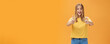 Woman supports with raised thumbs up and amused cheerful smile showing positive attitude expressing like on concept or idea giving approval posing happy and delighted against orange background