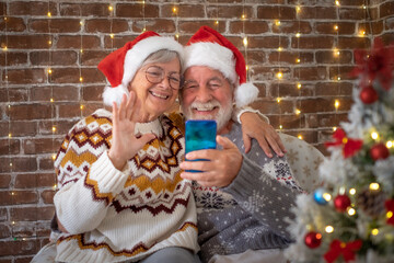 Wall Mural - Smiling senior adult couple sitting at home at Christmas time in video call with family or friends. Lovely elderly man and woman stay together at celebration event